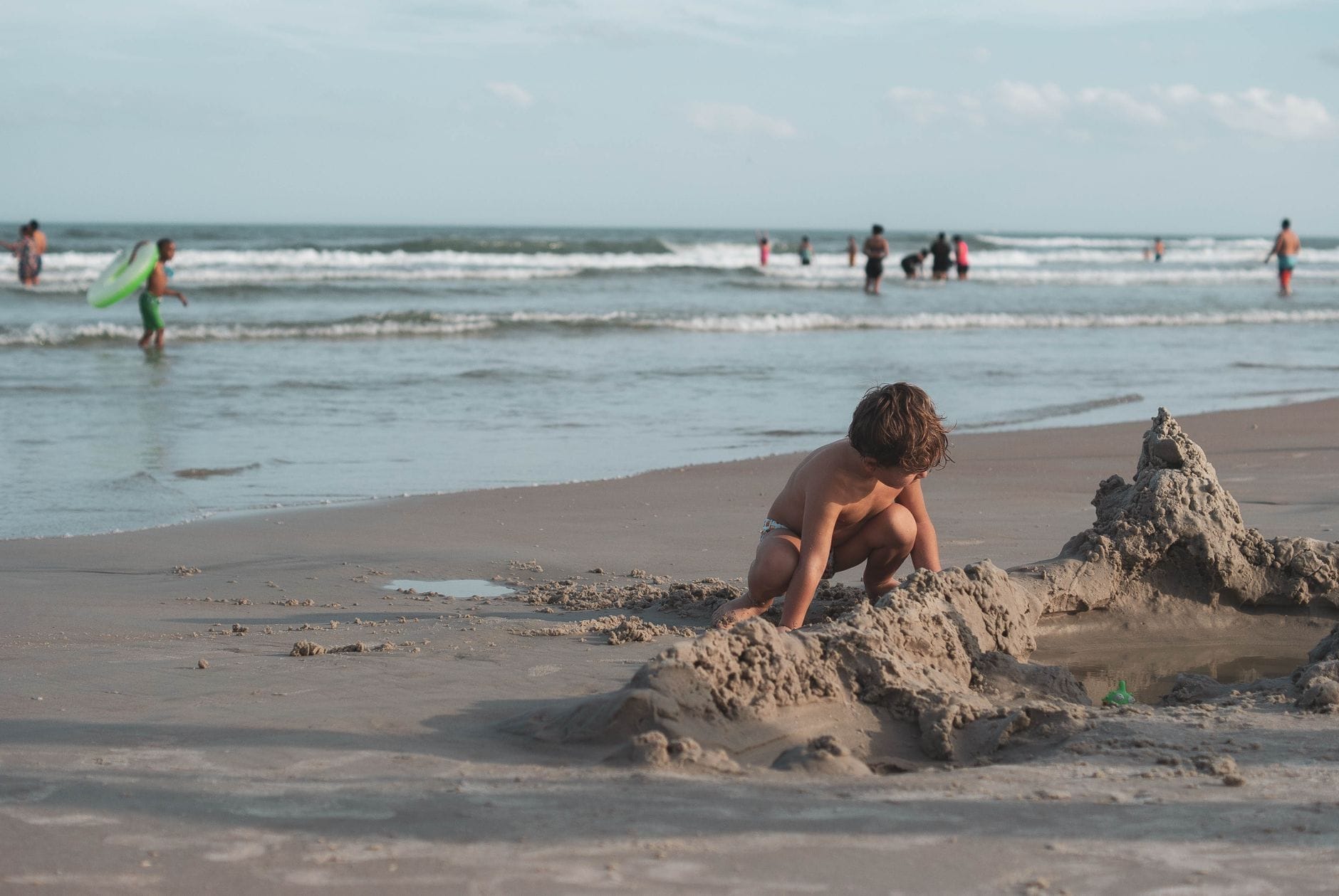 Chłopiec w kąpielówkach buduje zamek z piasku na plaży nad morzem