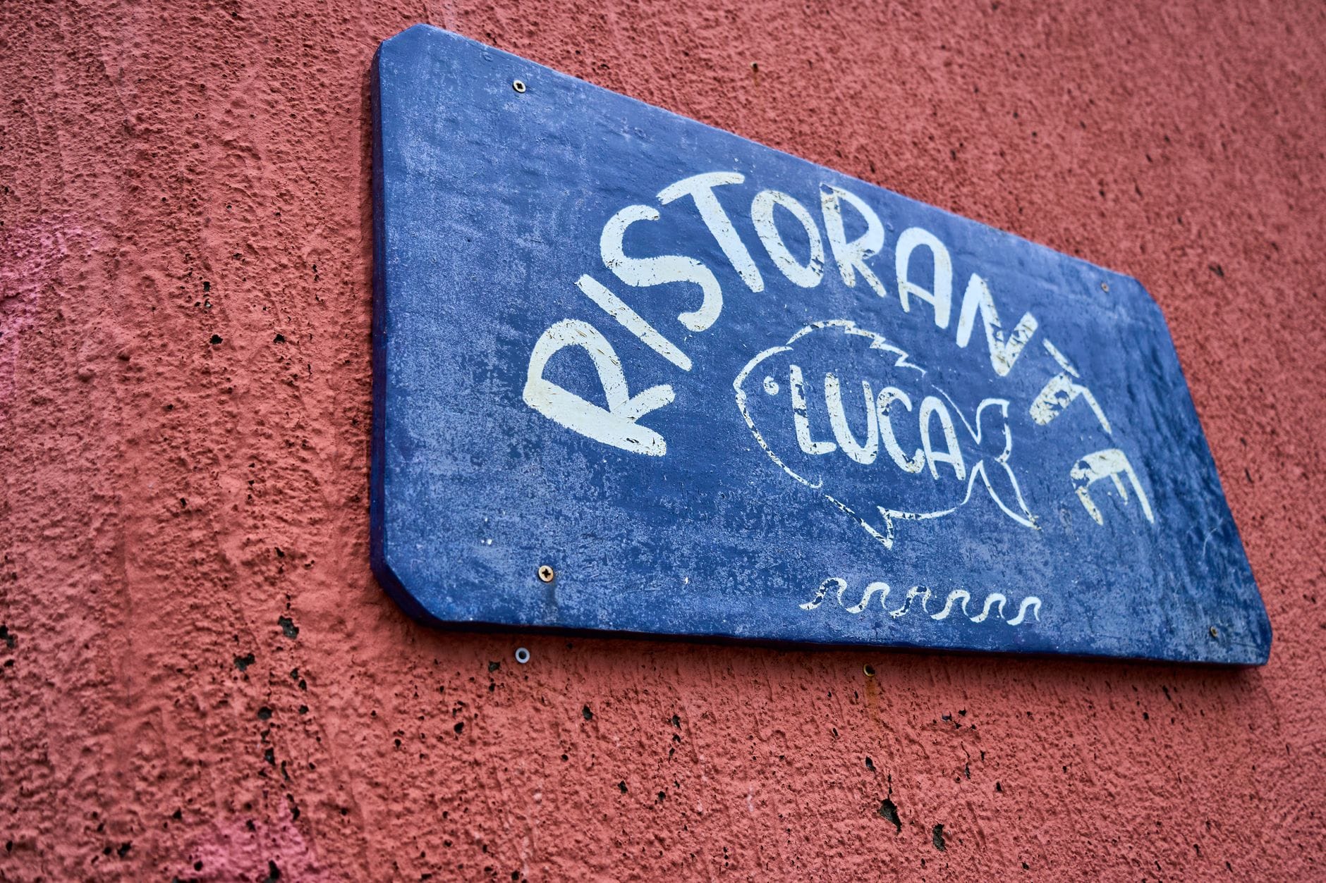 Niebieski szyld restauracji Luca z rybą na czerwonej ścianie